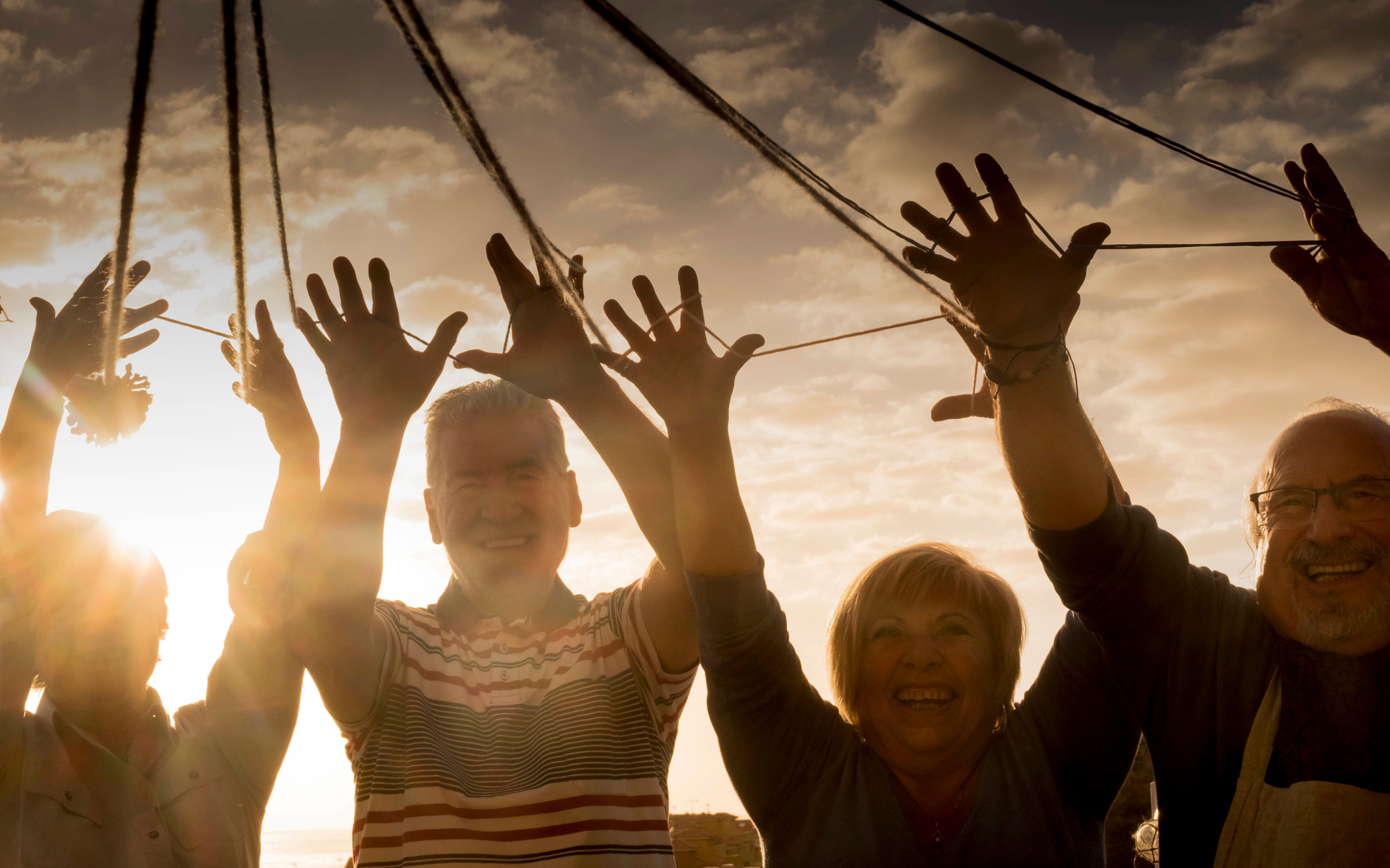 Ryhmä ihmisiä pitelee naruista auringonlaskussa