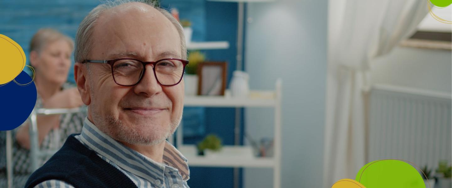 Hymyilevä silmälasipäinen hieman kalju vanhempi mies katsoo kohti